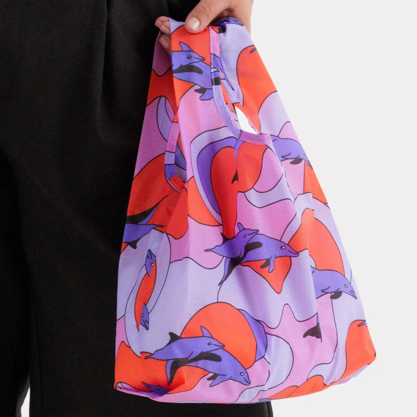 Baggu baby tote bag held by hand, dolphin print in purple, orange, and blue