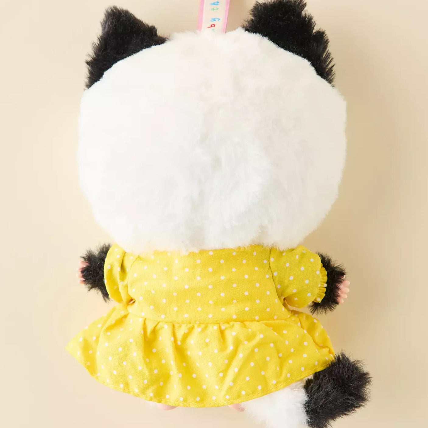 Cat keychain plush with white furry back and yellow dotted dress; black paws and key ring