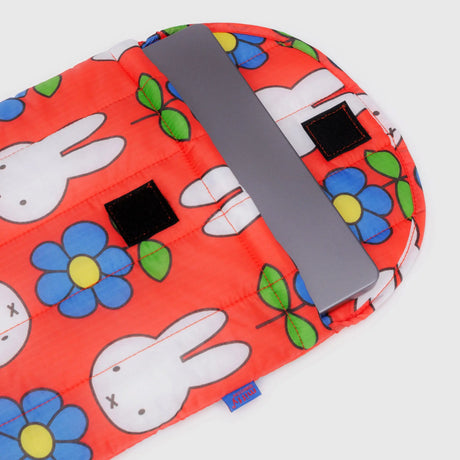 A silver laptop partially inside a red Baggu Miffy x Baggu Puffy Laptop Sleeve 13"/14" with cartoon bunnies, blue flowers, and two black velcro closures.