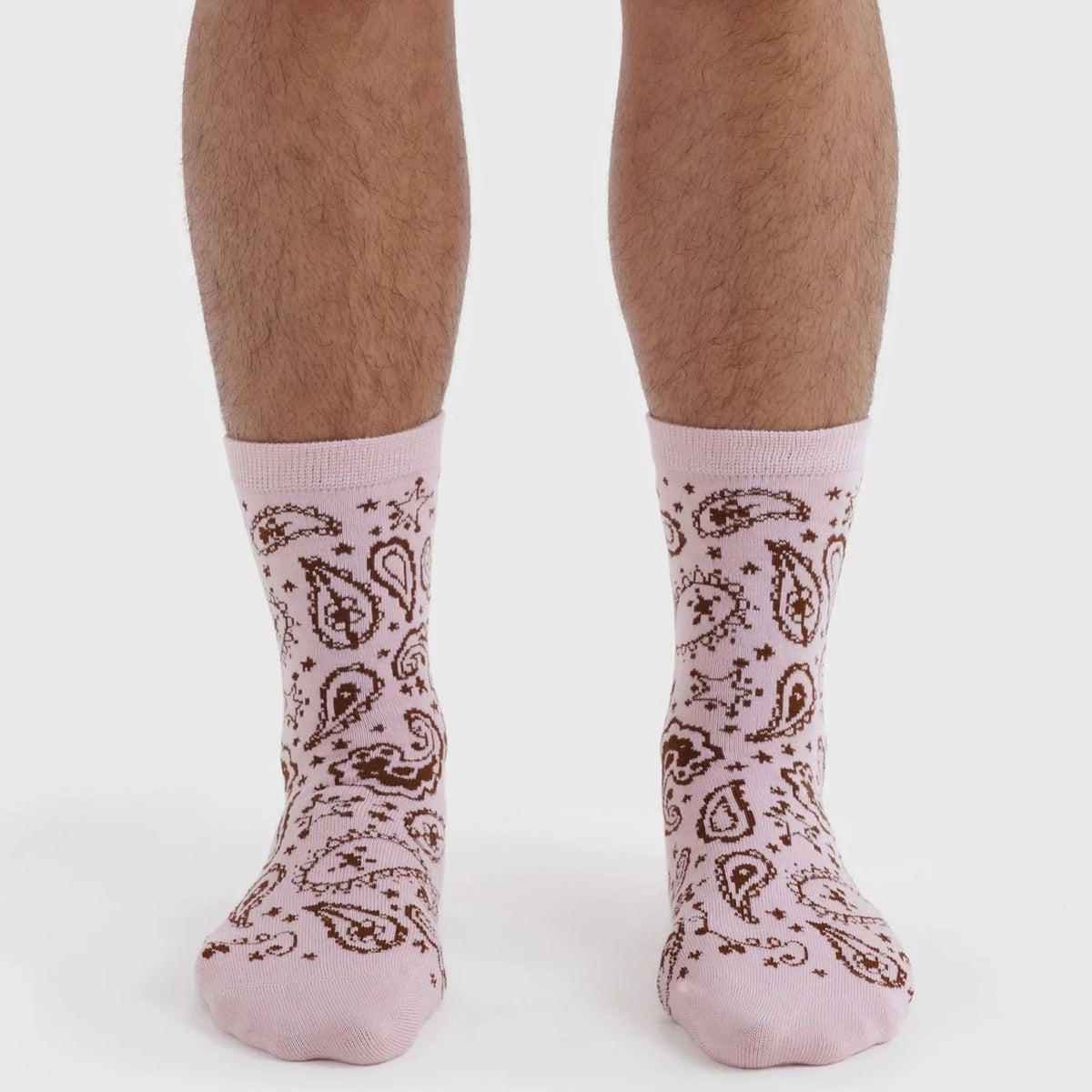 Pink crew socks with brown paisley and star pattern, pair shown on feet