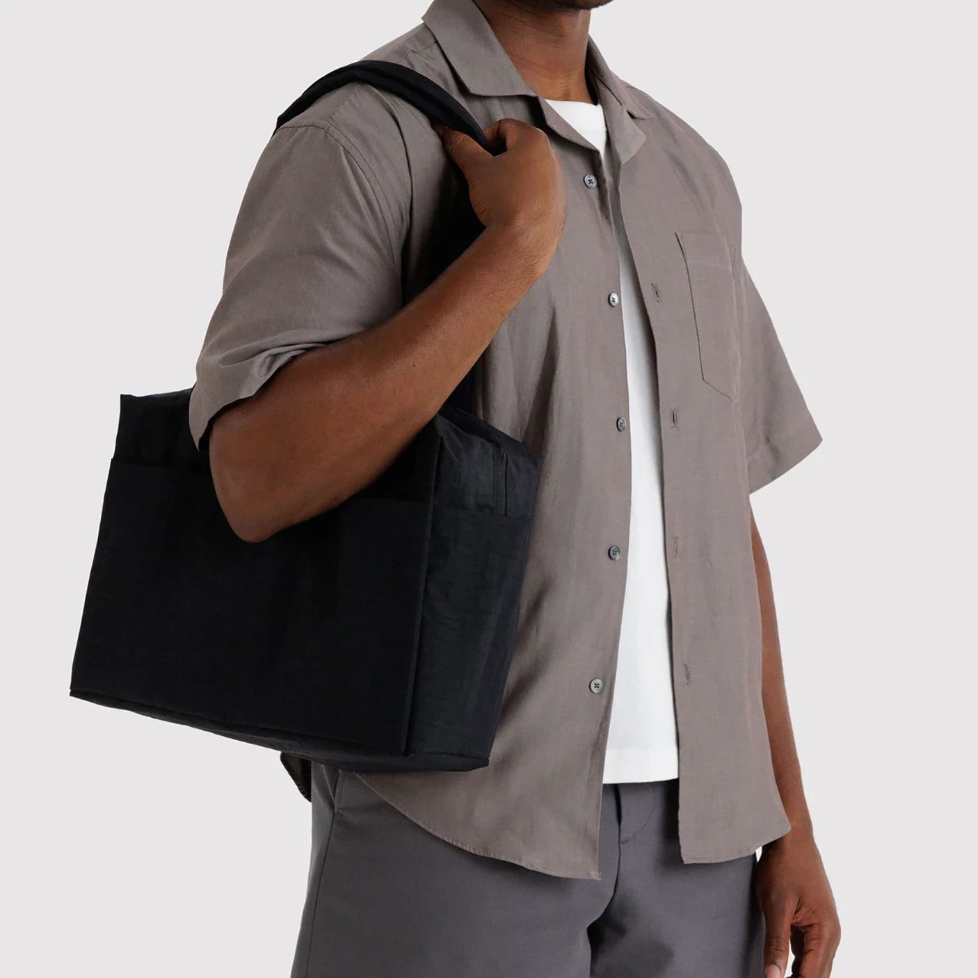 Man carrying solid black rectangular tote bag with double handles and exterior zipper pocket on shoulder