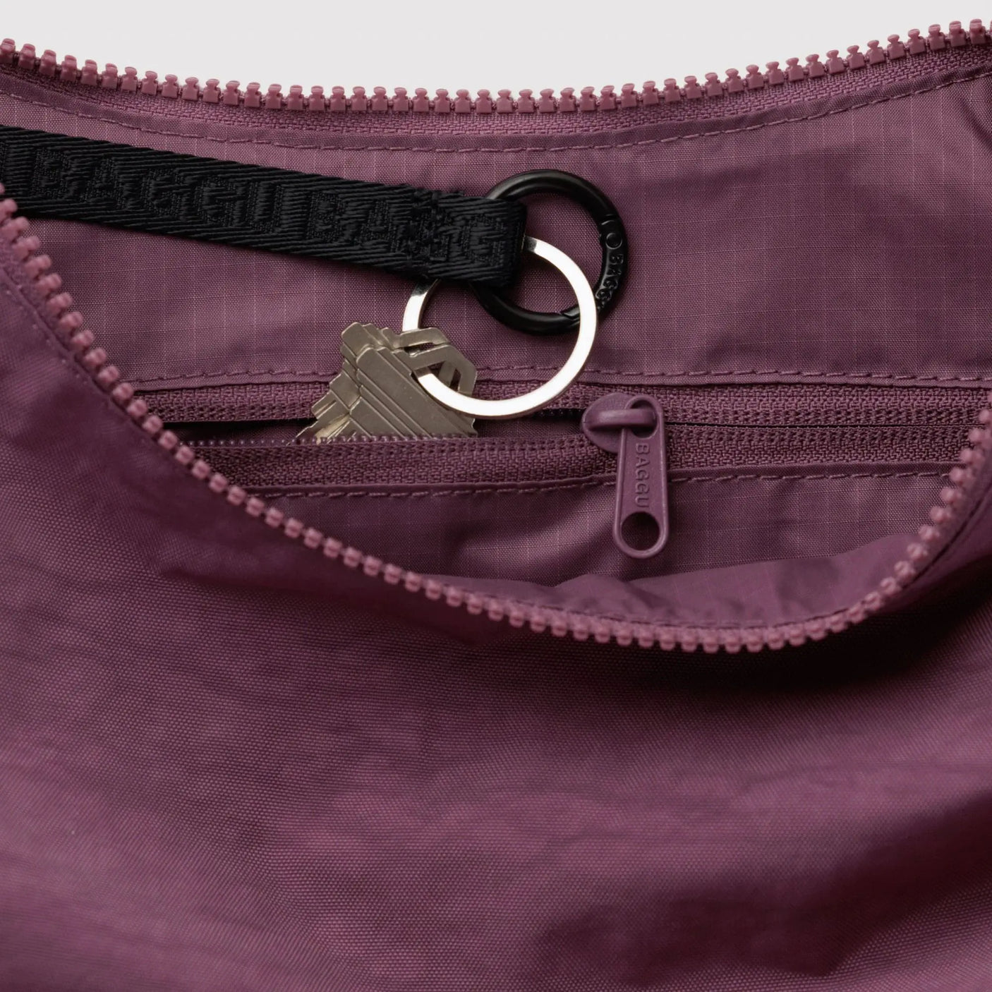 Wild plum nylon crescent bag interior with zipper, key ring, and dangling zip pull tab