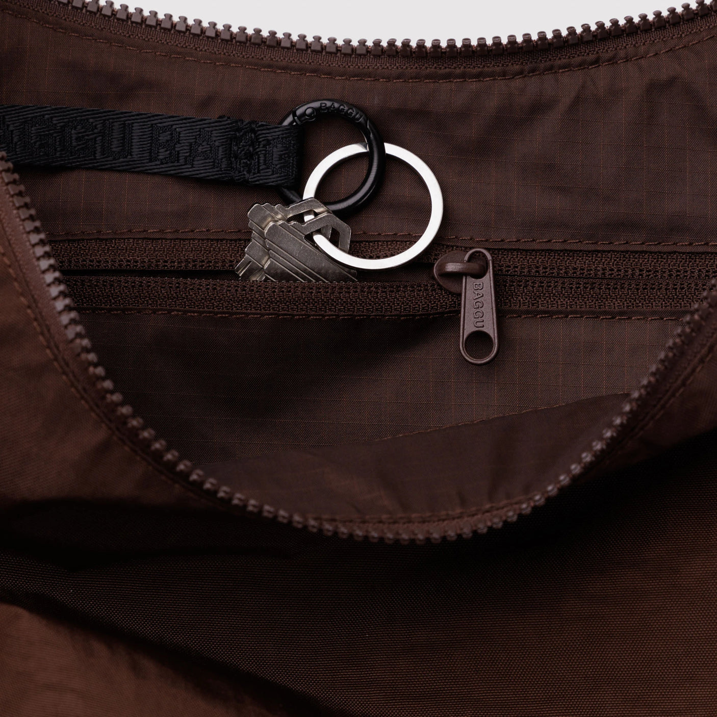 Close-up of dark brown fabric inner pocket with zipper and attached black key strap holding two silver keys