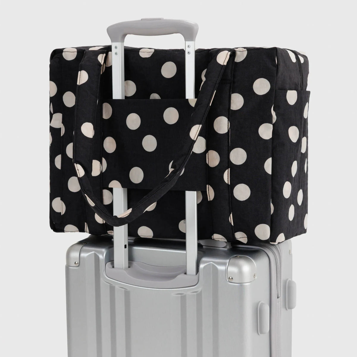 Polka-dot tote bag with cream dots, secured over a carry-on suitcase
