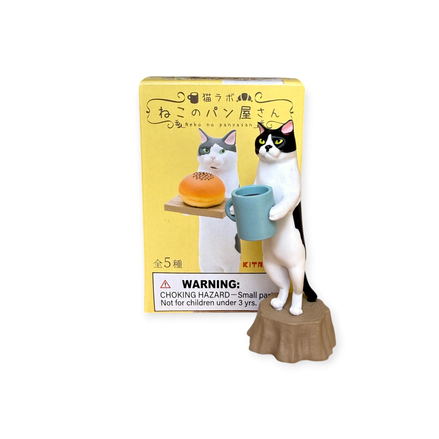 The Cat Bakery Waiter Blind Box by Kitan Club features a black and white cat figurine as a bakery waiter, holding a blue mug on a tree stump. The box shows treats next to the cat. Includes choking hazard warning.