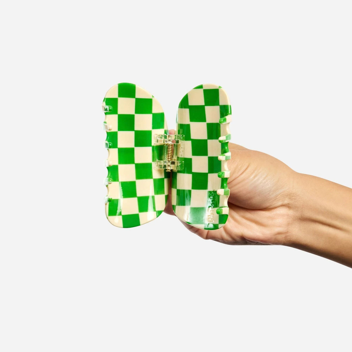 Green and white checkered claw clip, open prongs held in hand