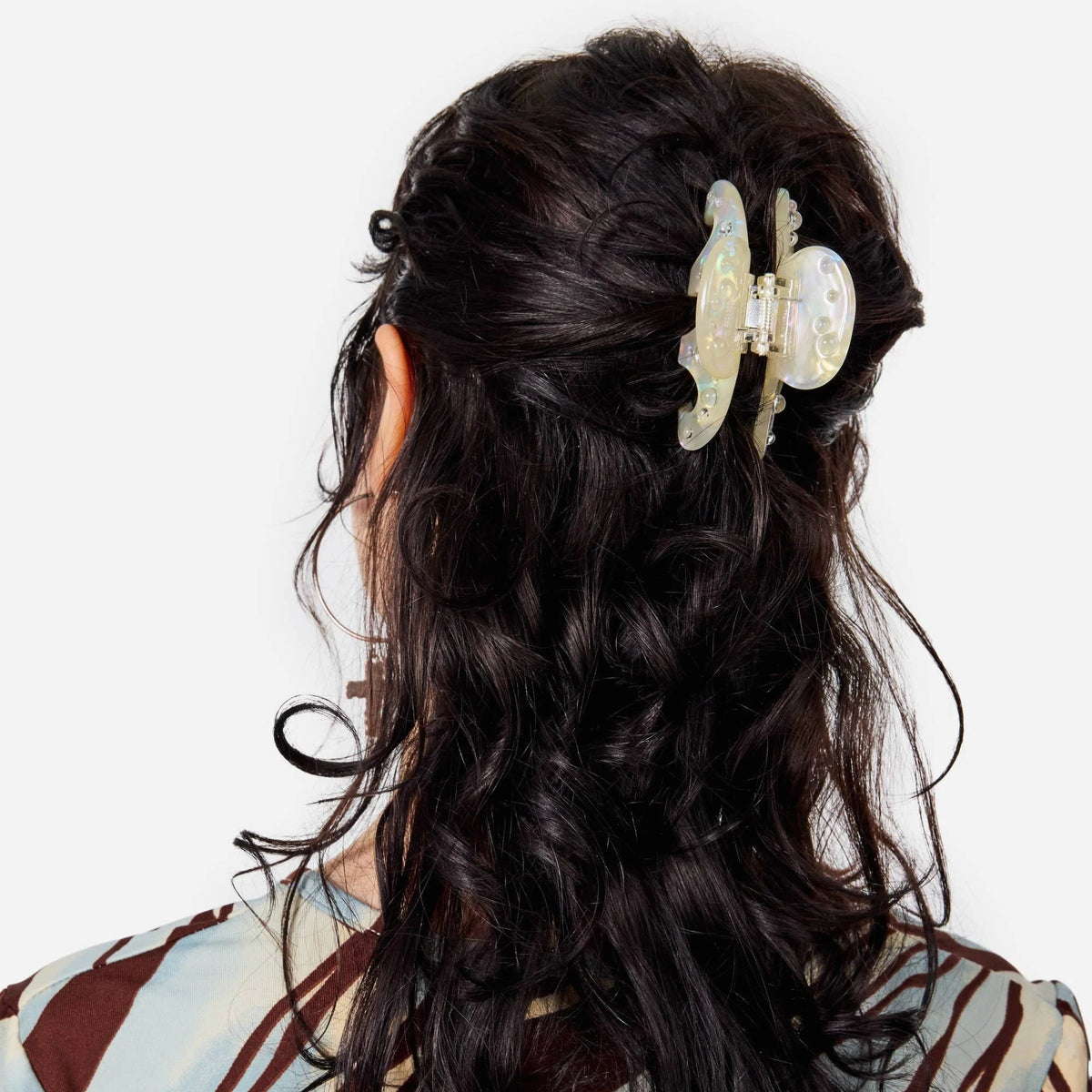 Octopus claw hair clip in translucent pearl-shimmer cream on dark wavy hair.