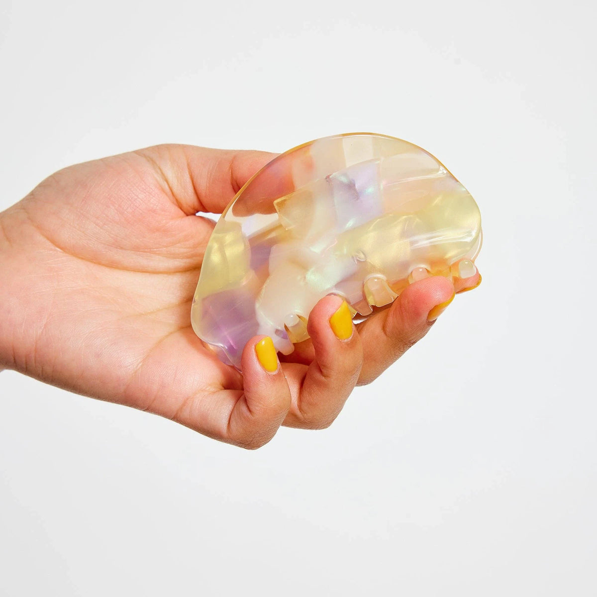 Pastel iridescent claw clip with curved teeth, held open in hand