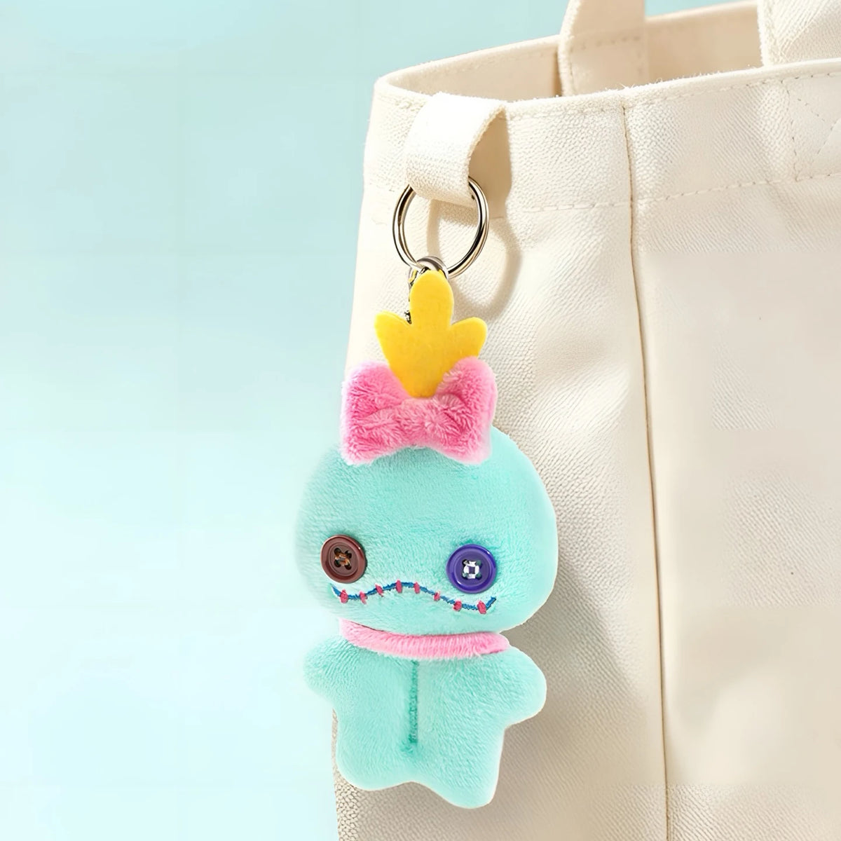 Teal plush character charm with pink flower topper and metal key ring on a tote.