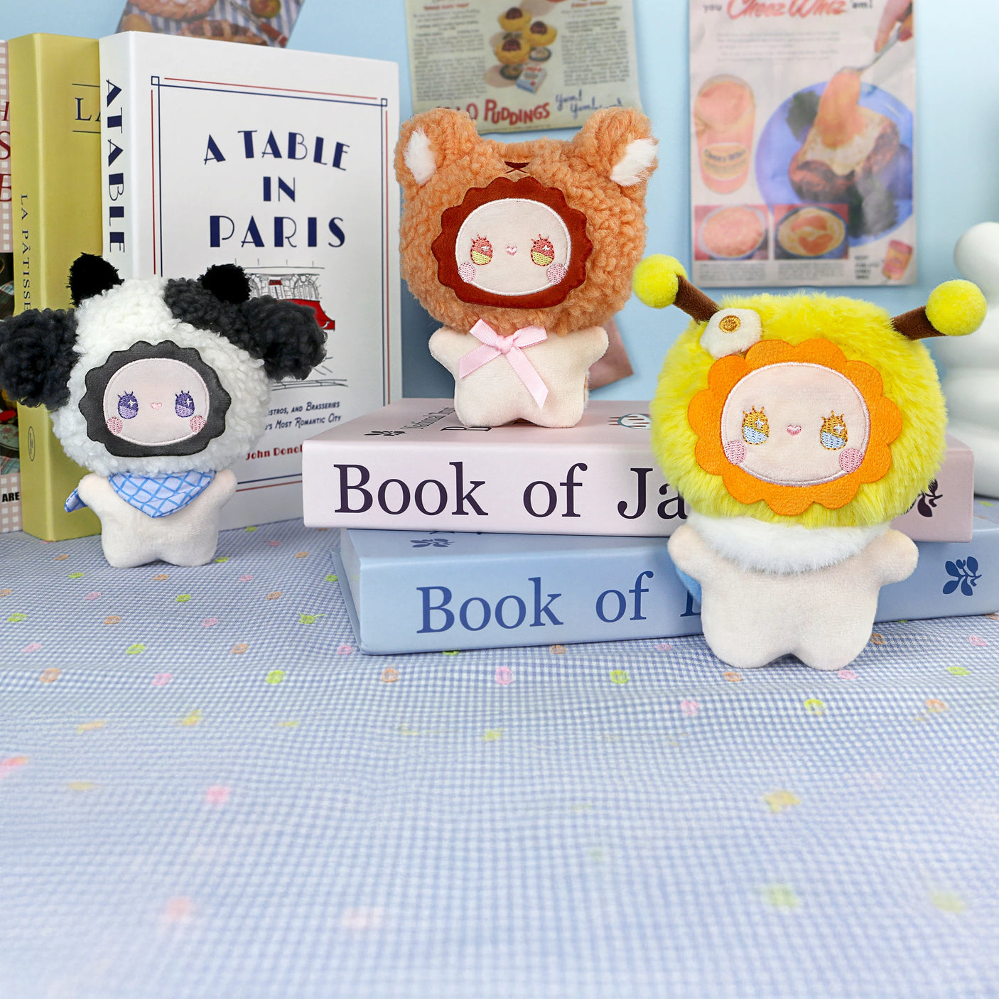Three plush dolls from the Lucky Emma Emma Fuzzy Family Bag Charm - Blind Box are displayed on stacked books, with more books upright in the background—perfect as a surprise charm or adorable accessory.