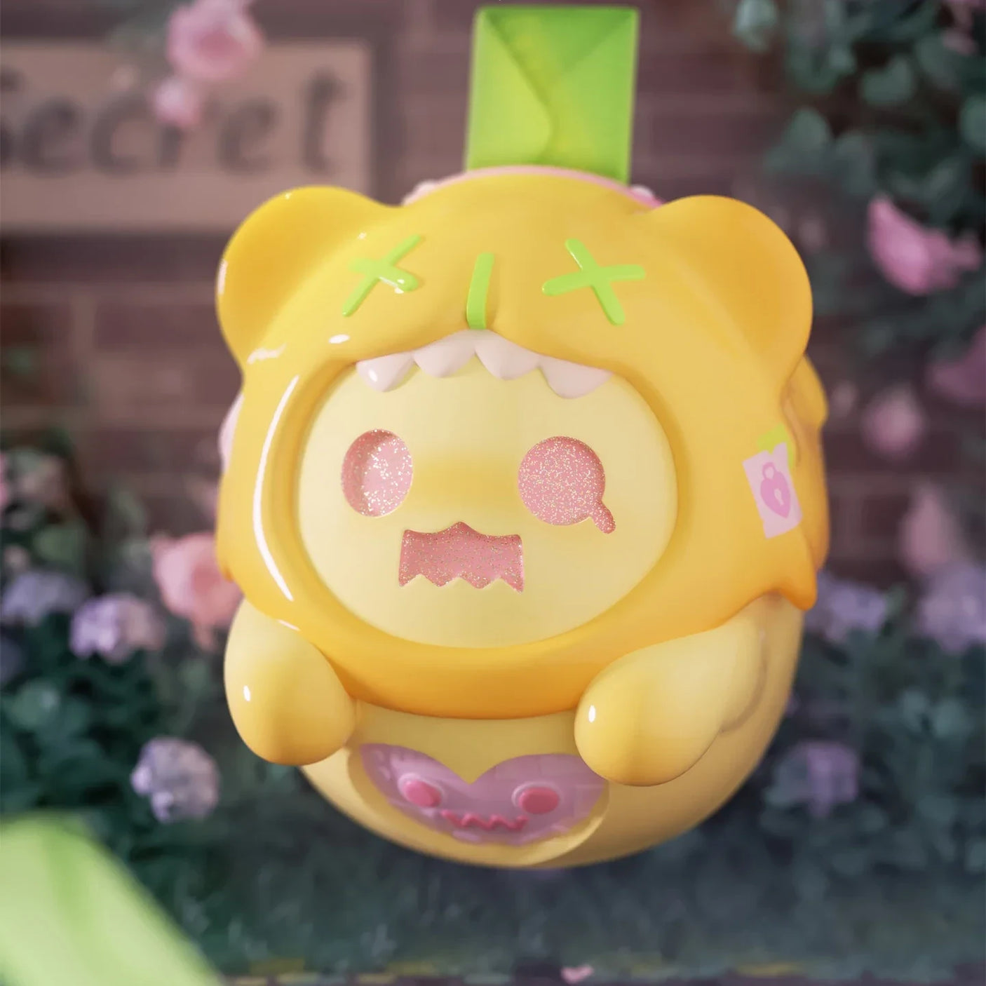 Glossy yellow ShinWoo Secret Bear figure with stitched eyes and pink sparkly face holding small purple accessory in garden setting