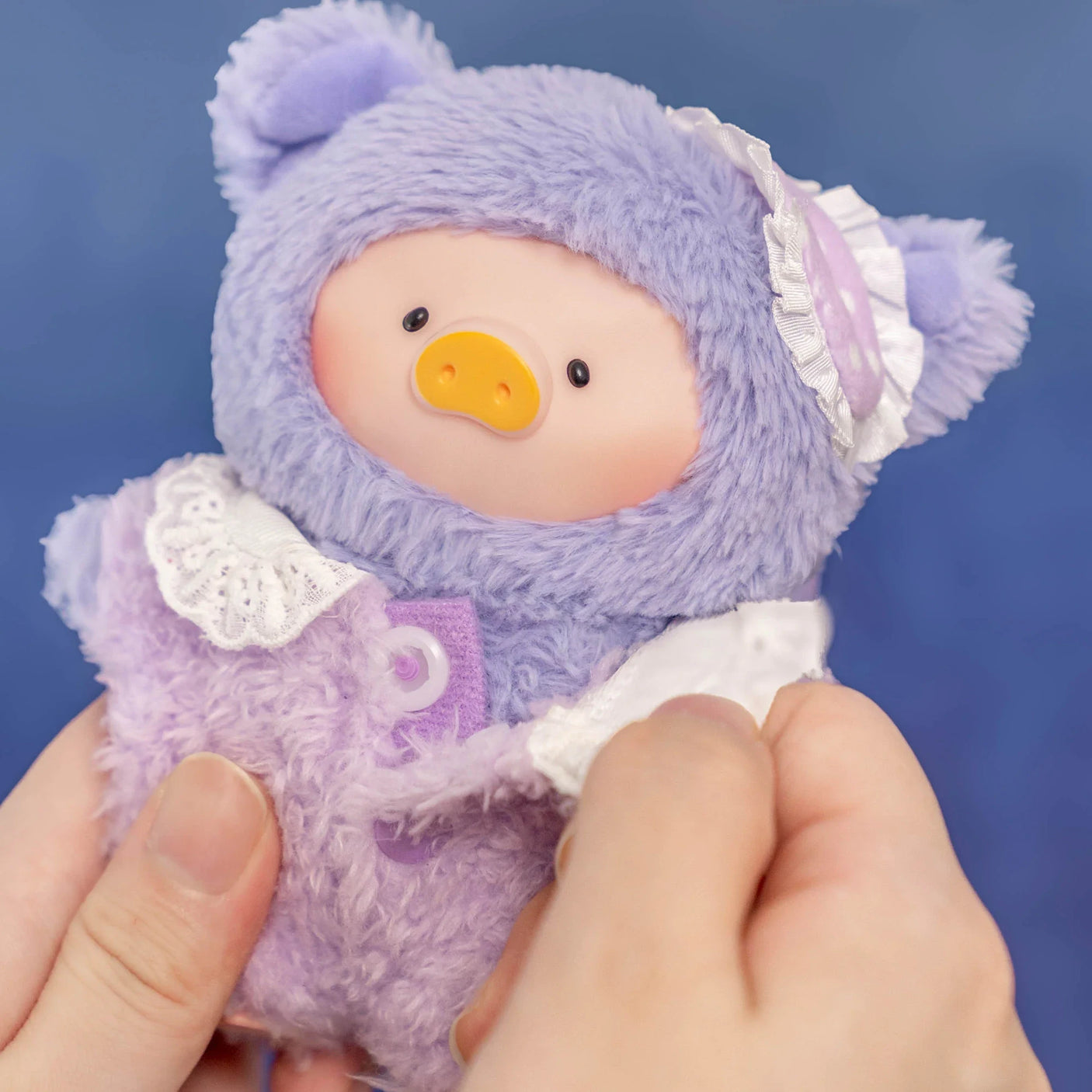 Close-up of Dreaming Wonderland LuLu Piggy plush keychain dressed in purple fuzzy pajamas with lace details held by hands
