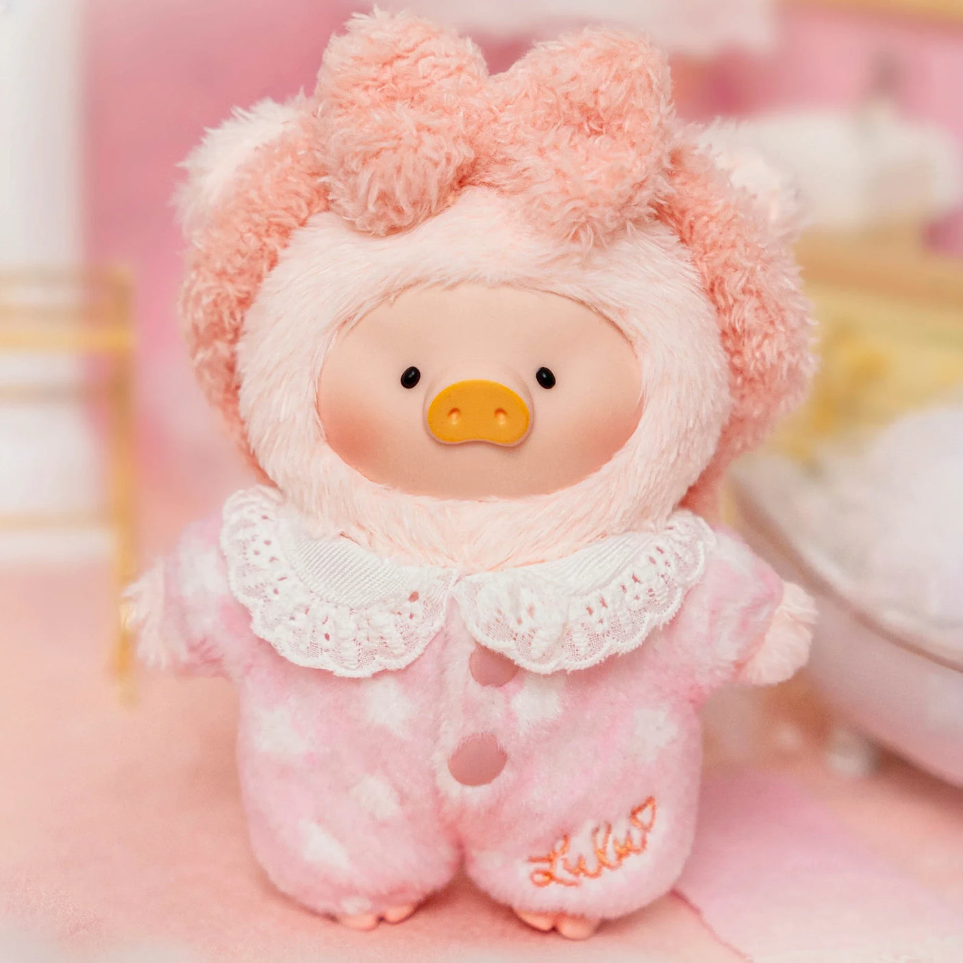 Soft LuLu Piggy plush doll wearing pink heart pajamas with lace collar and fluffy hood in cozy bedroom setting