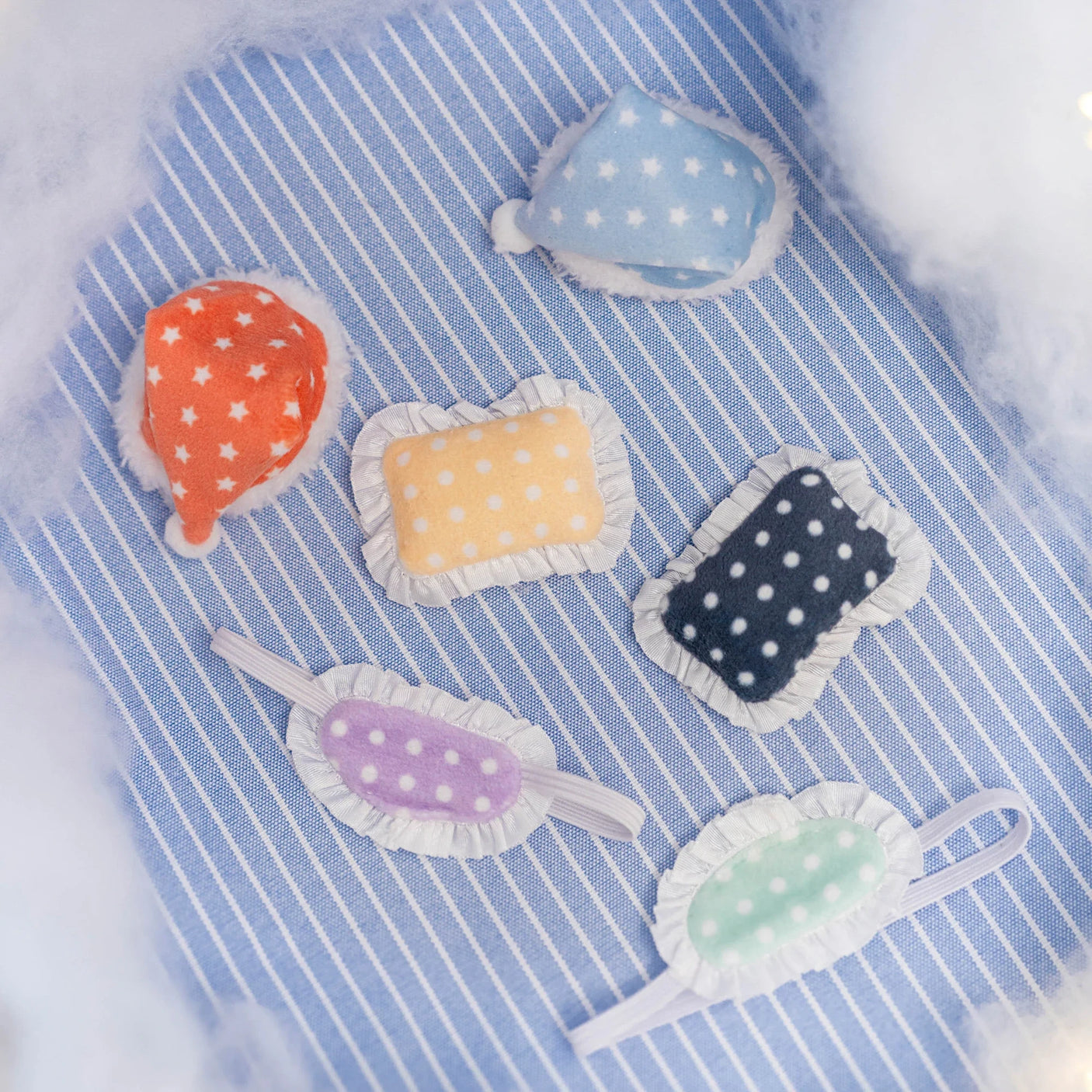 Colorful polka dot plush sleep masks and caps with ruffled edges arranged on striped blue fabric background