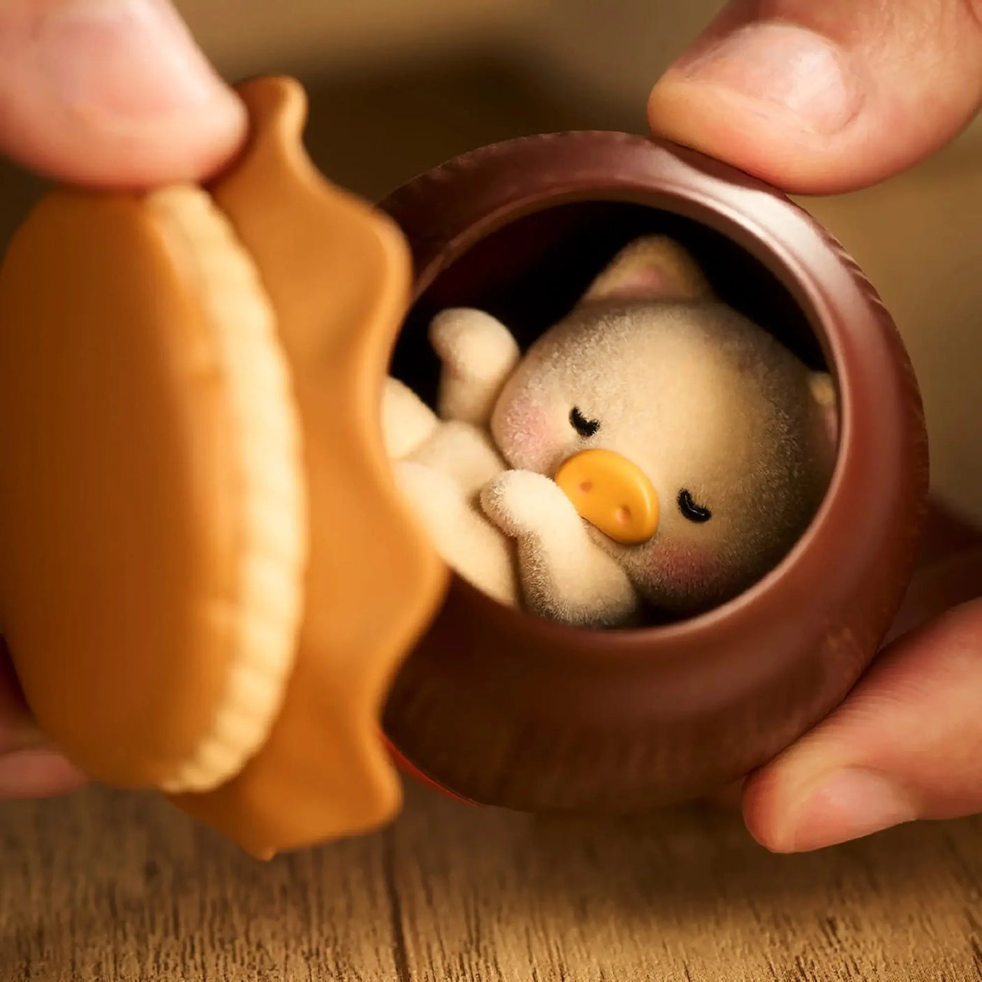 Brown pot container open to reveal a sleeping piggy figure inside, held by hands