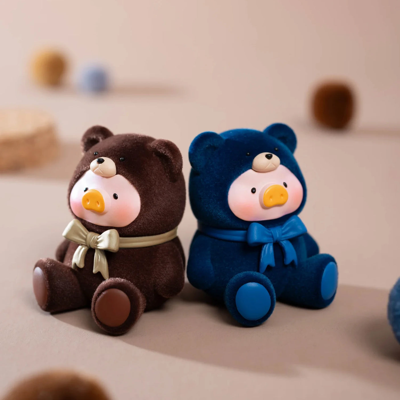 Two plush bear figurines—one brown with a beige bow, one blue with a blue bow—sit together, ideal for fans of collectible surprises like LuLu The Piggy - Mini Teddy Blind Bag from LuLu The Piggy.