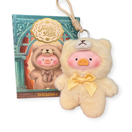The LuLu The Piggy "Teddy LuLu the Piggy Plush Pal - Blind Box" keychain wears a yellow teddy bear onesie with a bow, displayed in front of matching LuLu The Piggy and TOYZERO+ packaging. A perfect collectible!