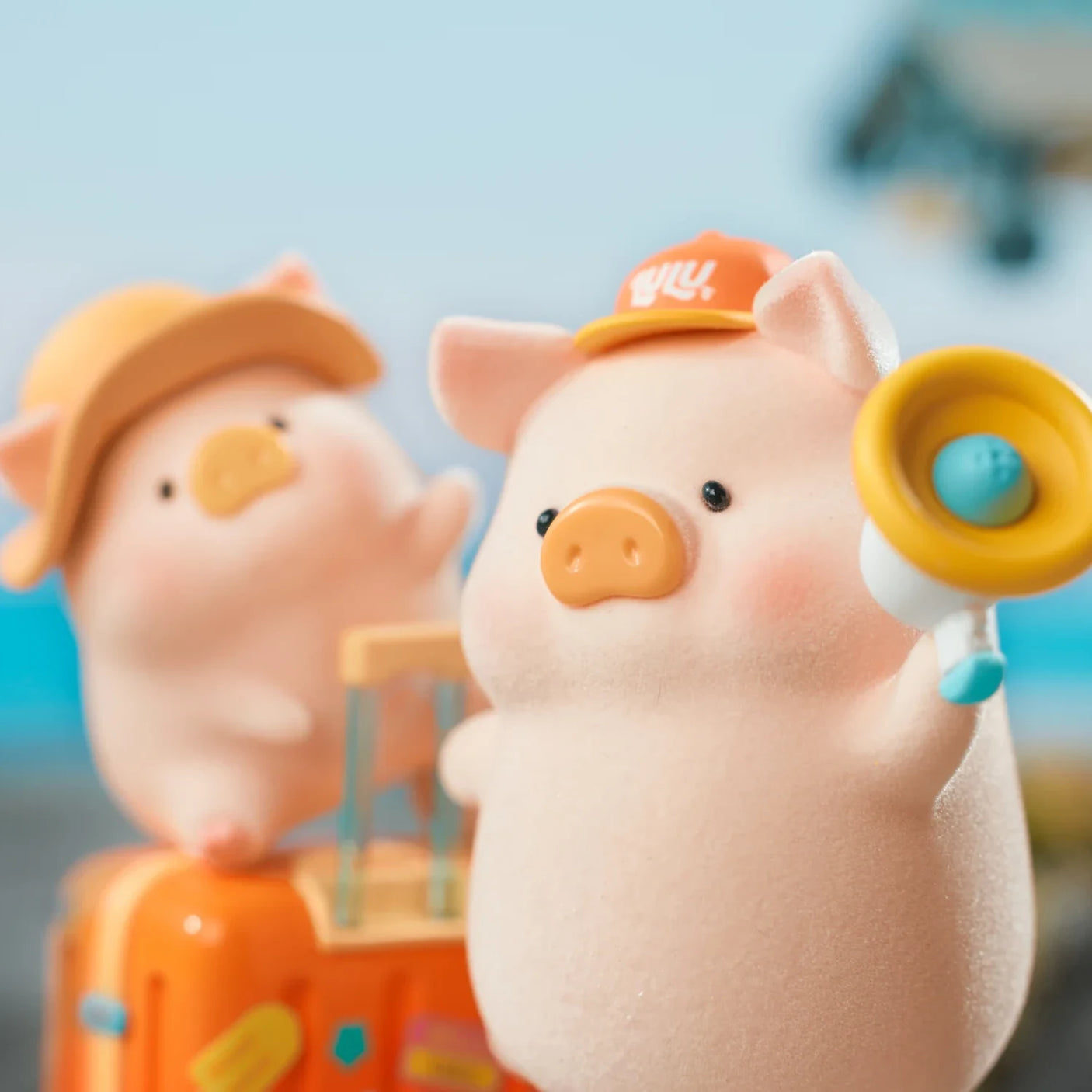 Chubby LuLu the Piggy holding a yellow megaphone wearing an orange cap with another LuLu and suitcase in background