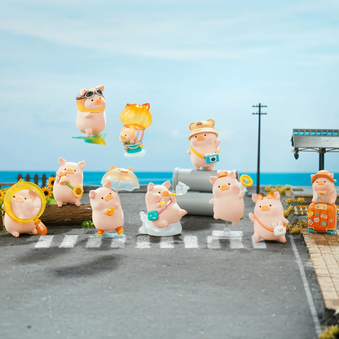 Collection of LuLu the Piggy travel-themed figures posed with accessories on a miniature street and seaside background