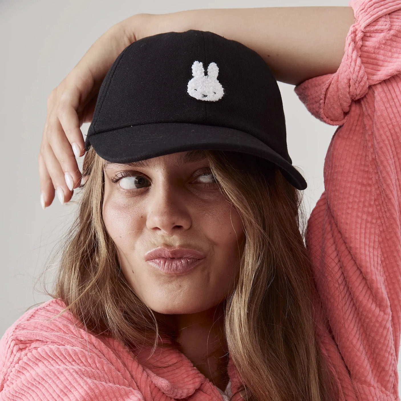 Black baseball cap with white bunny applique, worn by a woman