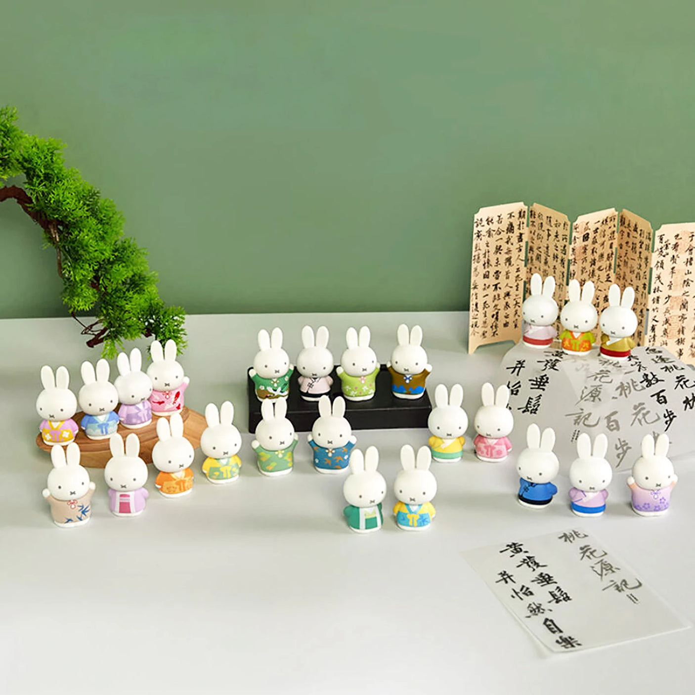 Set of 21 Miffy figures in colorful ancient-inspired costumes arranged with calligraphy scrolls and greenery background