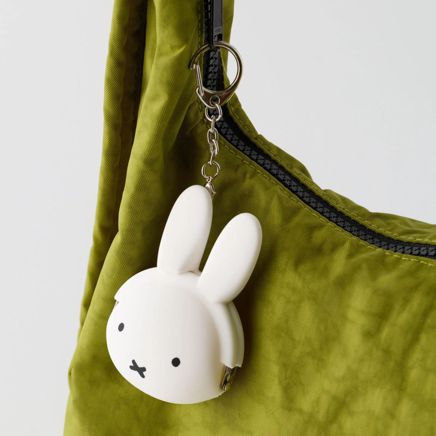White Miffy keychain coin pouch made of soft silicone hanging from an olive green bag zipper pull.