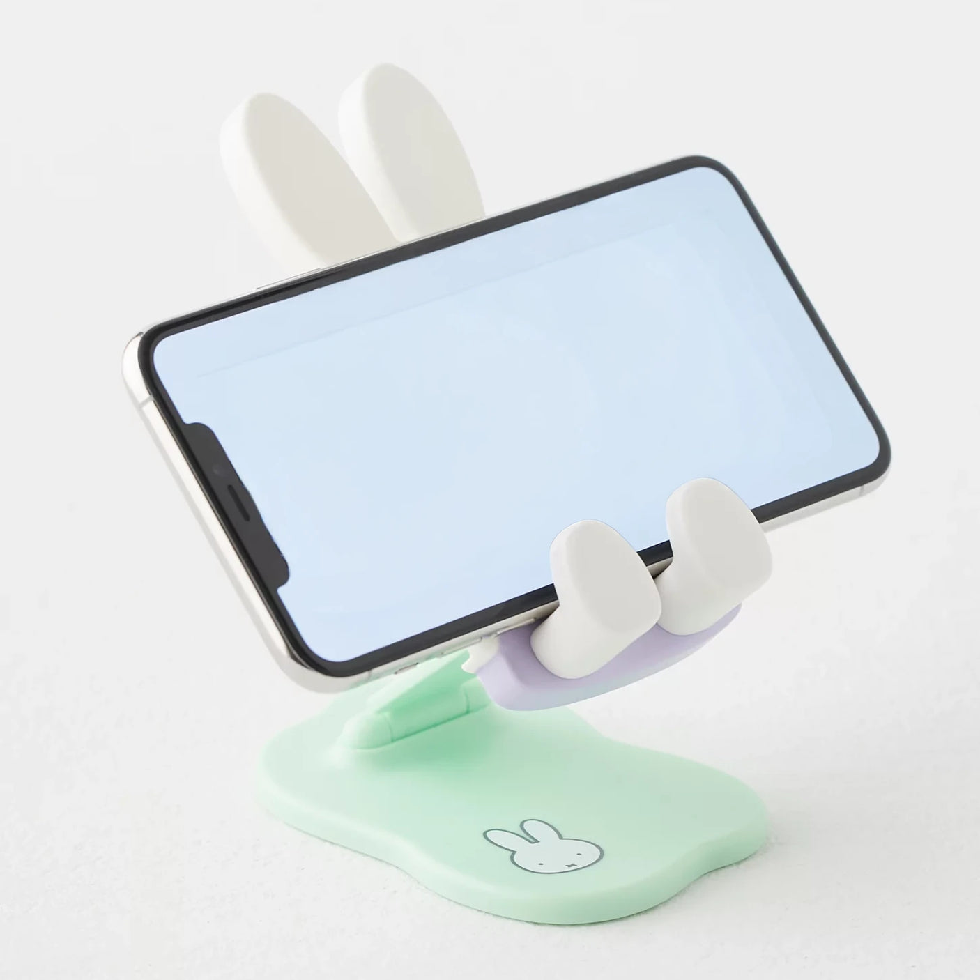 Pastel green Miffy phone and tablet stand with white ears and hands holding a smartphone horizontally on white background