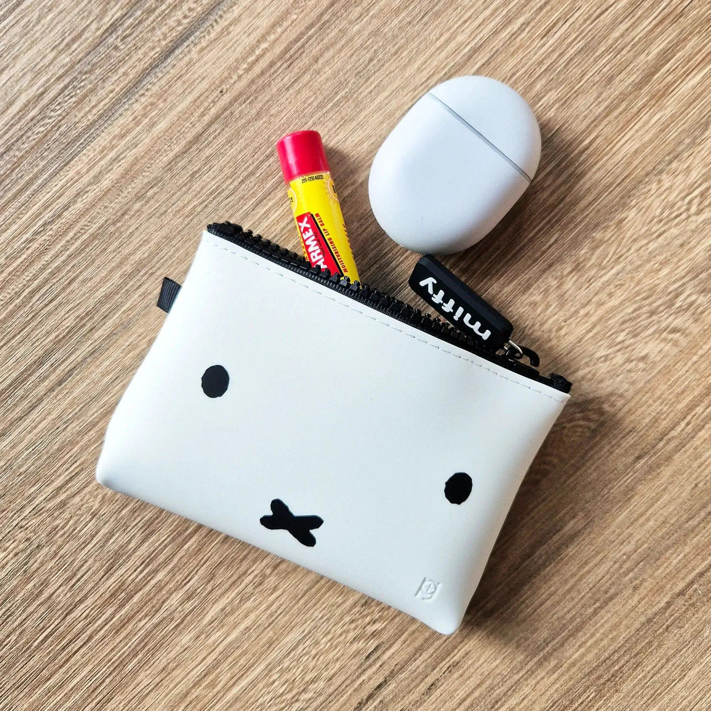 On a wooden surface sits the Miffy Bunny Case White - 14cm, showcasing its charming white silicone pouch with a cute face des