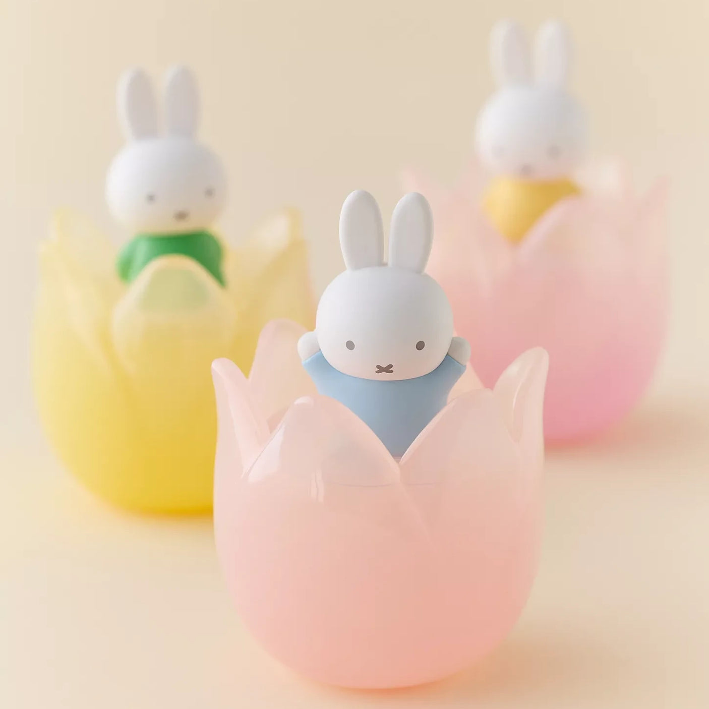 Three Miffy figurines dressed in pastel outfits sitting inside translucent tulip-shaped holders on soft background