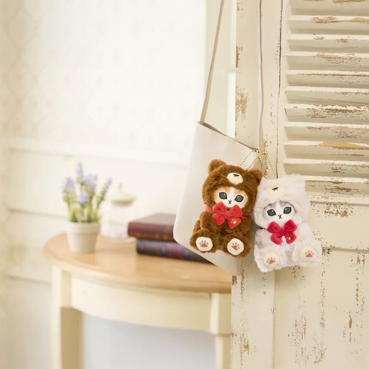 Two Mofusand plush cat keychains dressed in teddy bear suits with red bows hanging from white bag on rustic door