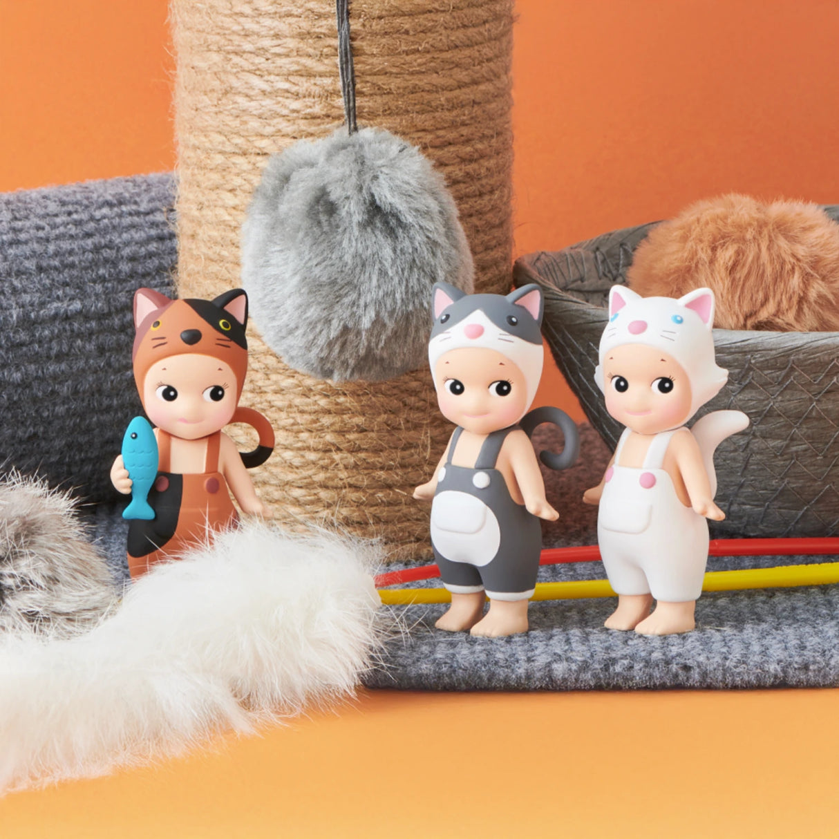 Three figures from the Sonny Angel Cat Life Series - Blind Box by Sonny Angel are dressed as cats and stand on a play surface adorned with a scratching post and fluffy objects, capturing the essence of this Limited Edition series.