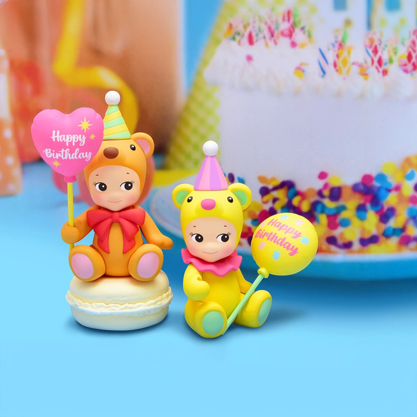 Two Sonny Angel Birthday Bear Gift figurines, wearing festive party hats and holding celebratory signs, are perched on a macaron with a vibrant birthday cake shining brightly in the backgroundβa delightful gift to charm any celebration.