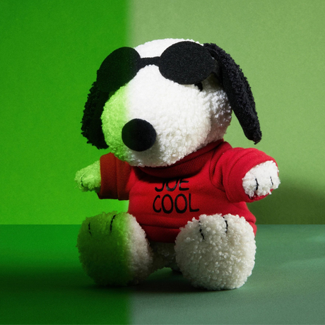 Snoopy plush wearing black sunglasses and red "Joe Cool" sweatshirt sitting against green background.