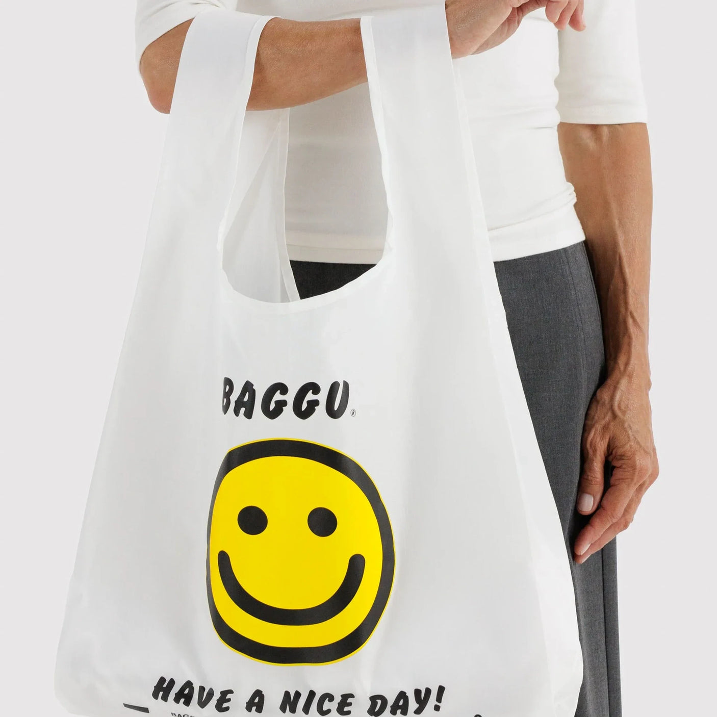 White tote bag held in hand, featuring Baggu smiley face and 'Have a nice day' quote