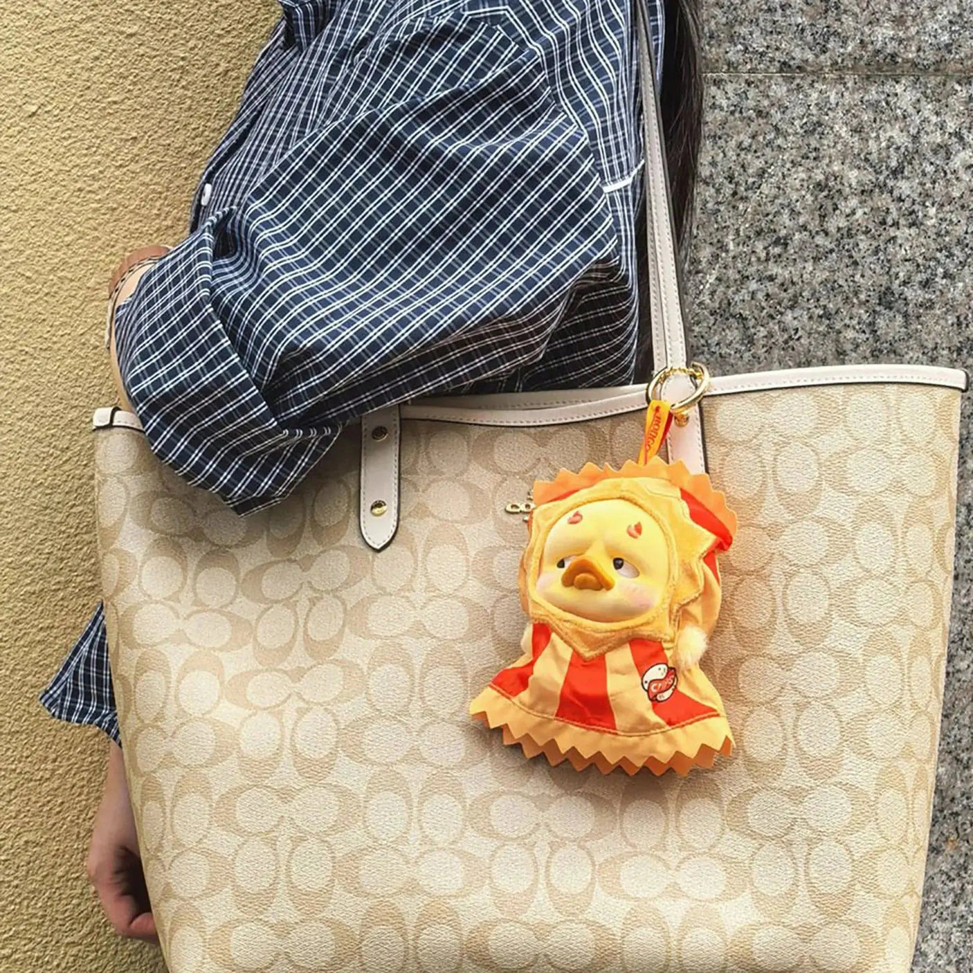 Vinyl plush duck charm in red circus outfit on a beige patterned shoulder bag.