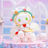 This cute cat-like figurine from Lucky Emma's hand-painted figures blind box series features green eyes, a translucent halo, floral wreath, and wings. It sits on a pink platform with arched windows and vibrant flowers, reminiscent of a Secret Forest Wedding.