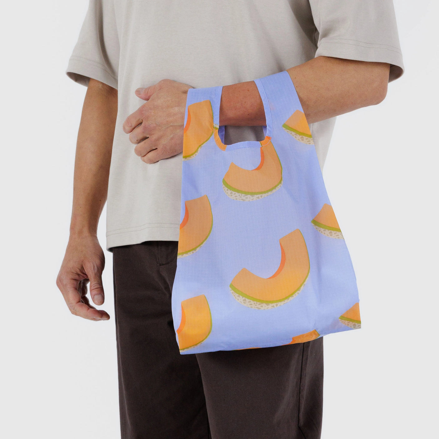 Someone is holding a Baggu Baby Baggu Reusable Bag in Cantaloupe Blue while wearing a beige shirt and dark pants.