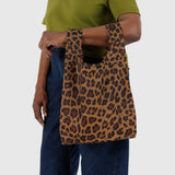 A person confidently carries the Baby Baggu Reusable Bag - Leopard by Baggu, effortlessly pairing it with a green top and blue jeans.