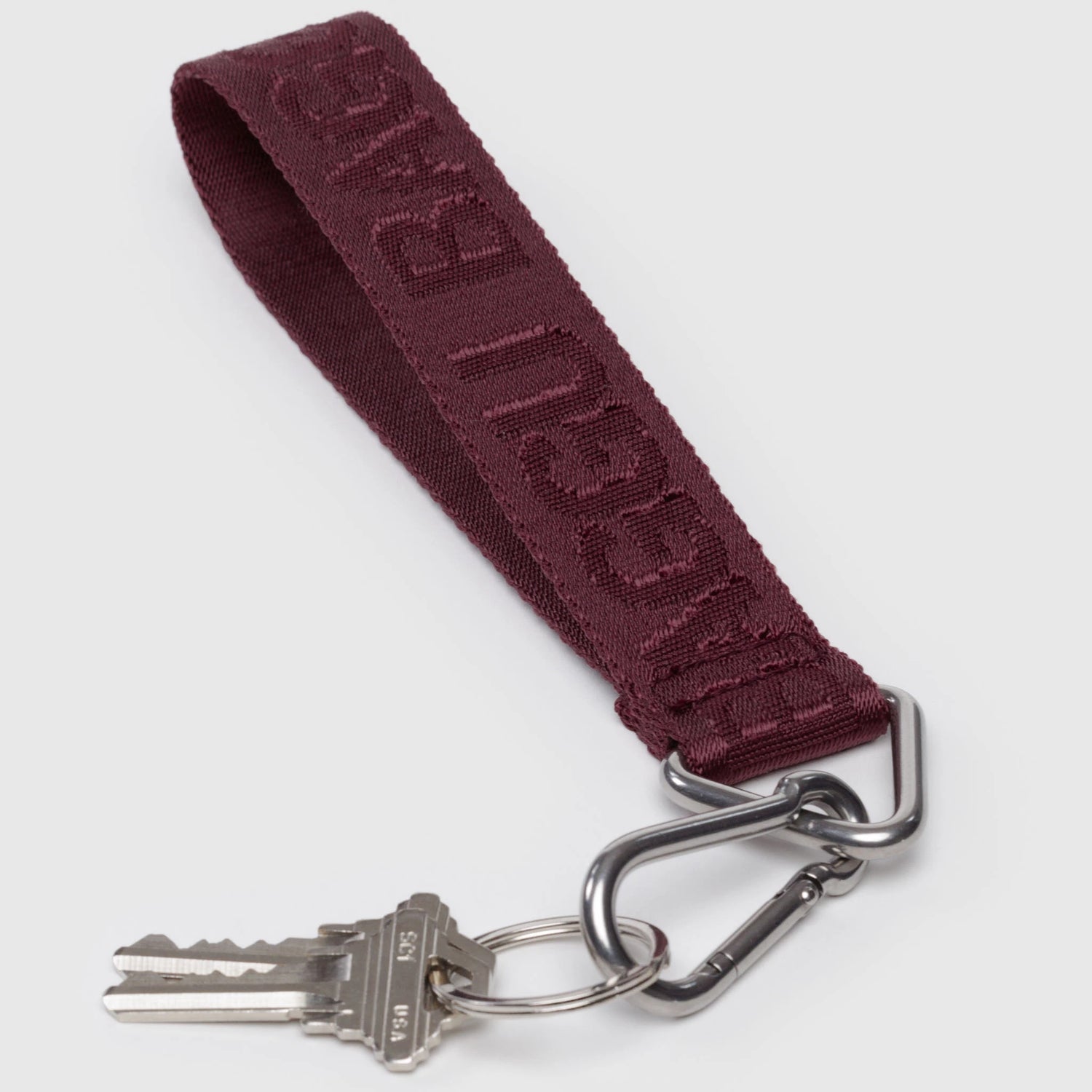 The Baggu Logo Keychain - Mahogany features embossed lettering on recycled nylon, attached to a metal keyring with two silver keys and a carabiner clip.
