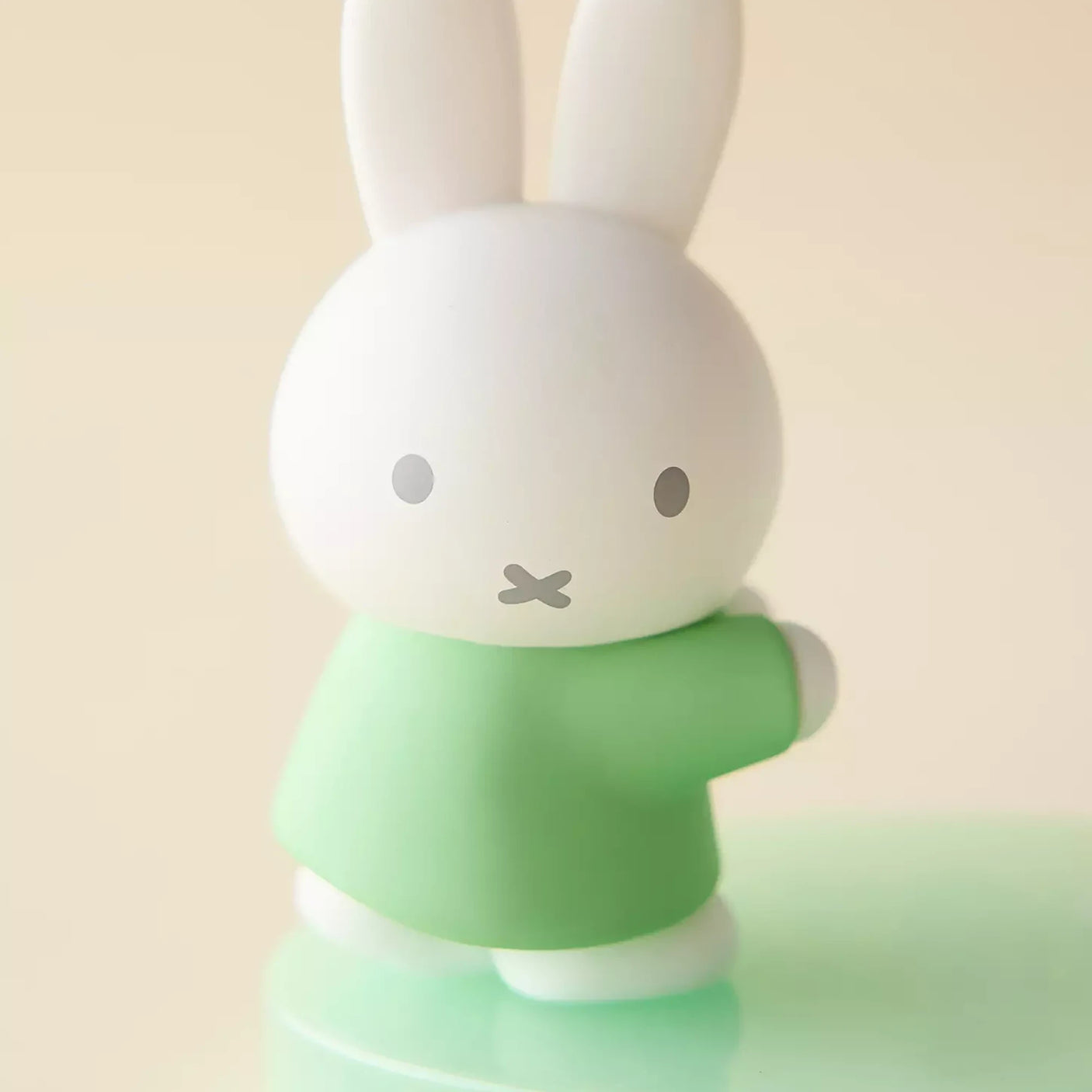 White bunny figurine with green shirt on light blue base phone stand, close-up