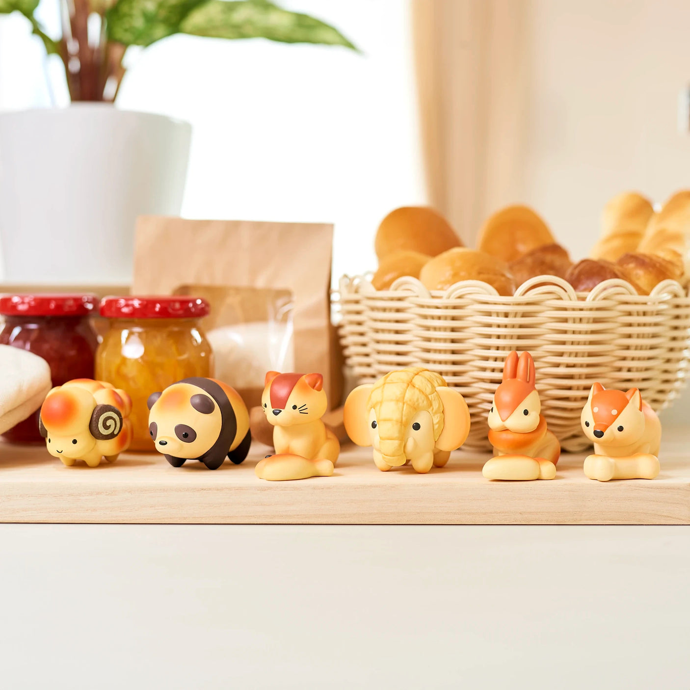 A line of Dreams Inc's Animal Bakery Mini Figure Blind Boxes graces the kitchen counter, with jars of jam and a basket of bread rolls in the background. These charming collectibles add a whimsical touch to any space.