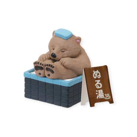 Bear figurine with blue head towel soaking in square onsen tub, paired with small wooden sign, gallery position 1