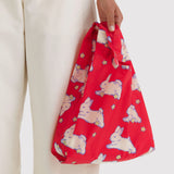 Person holding red reusable bag decorated with playful cream rabbits and small yellow flowers against white background