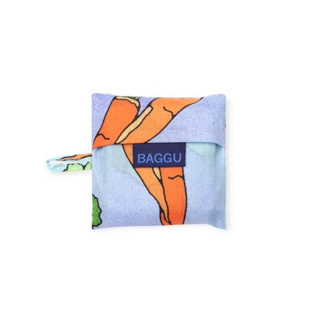 Folded reusable bag with orange carrot design and navy blue label on light blue fabric background