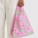 Light pink fabric bag with playful cream lamb illustrations and small scattered red flowers held by a person in white pants