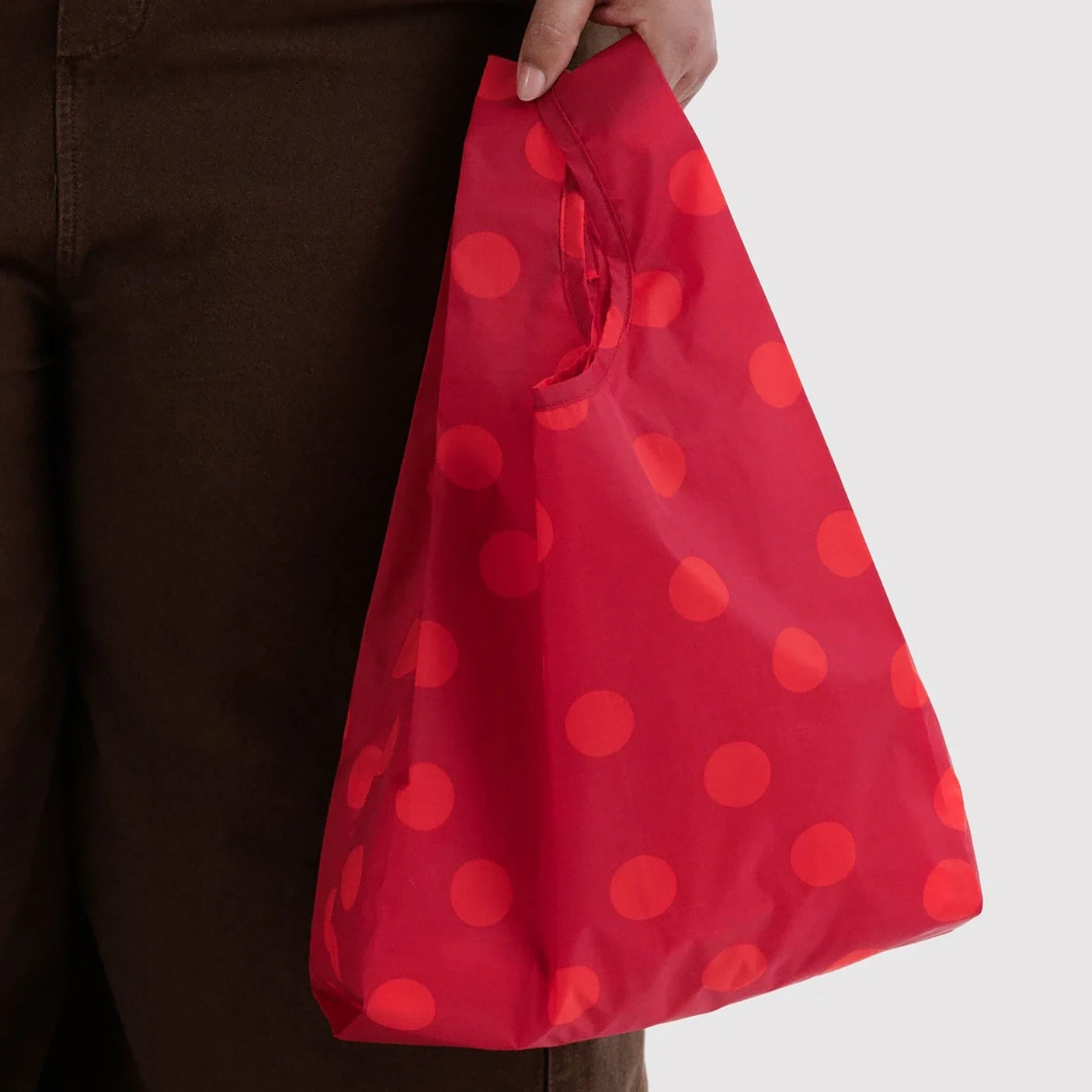 Red polka dot Baggu reusable tote bag, held open-top with small handles
