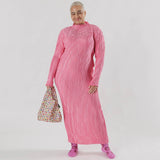 A person in a long, pink, pleated dress stands in the studio, holding a limited edition Baby Baggu Bag featuring Hello Kitty Icons and wearing pink socks with designs.