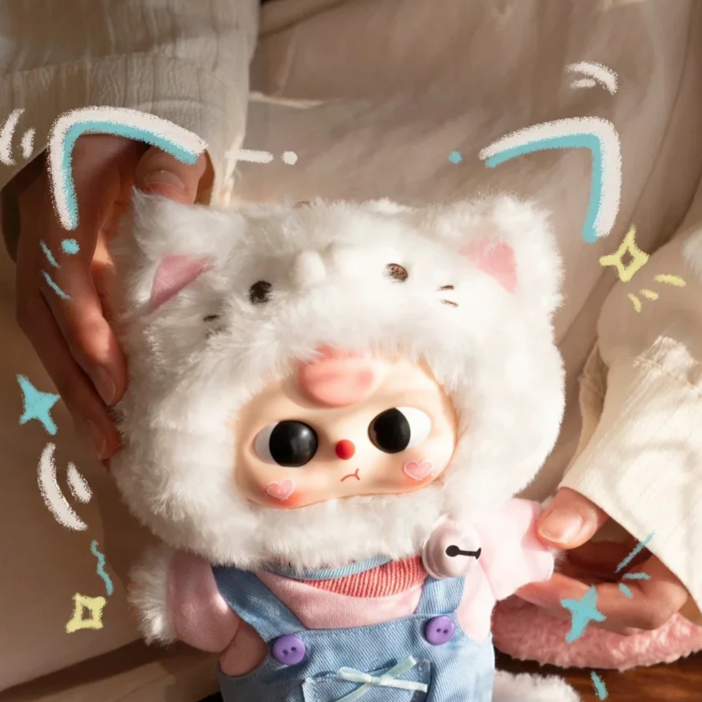 White plush kitten keychain with pink nose and blue-trim ears, held by hands
