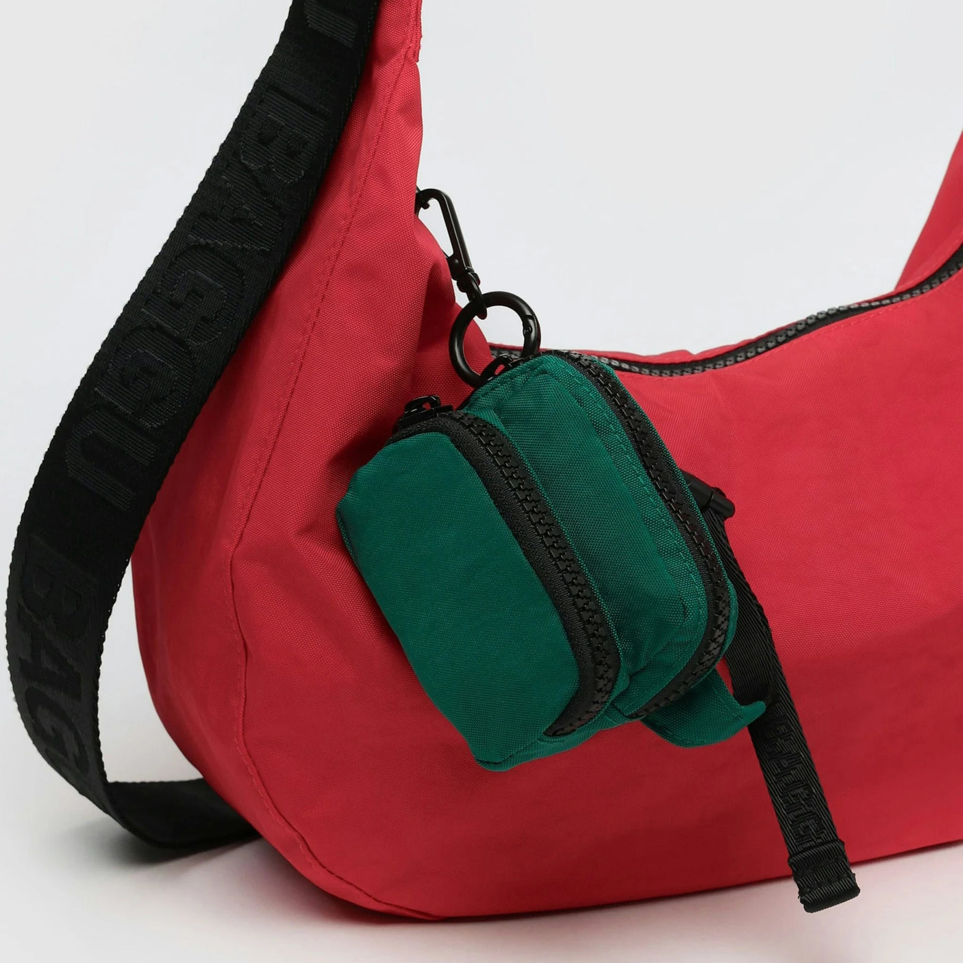 Red handbag with a black strap and an attached small green pouch, featuring the Baggu Fanny Pack Charm - Cypress for added flair.