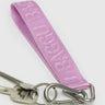 Close-up of the Baggu Keychain - Logo Strap showcasing a pink strap crafted from recycled nylon webbing and equipped with a metal clip, holding two keys. The eco-friendly strap features embossed text.